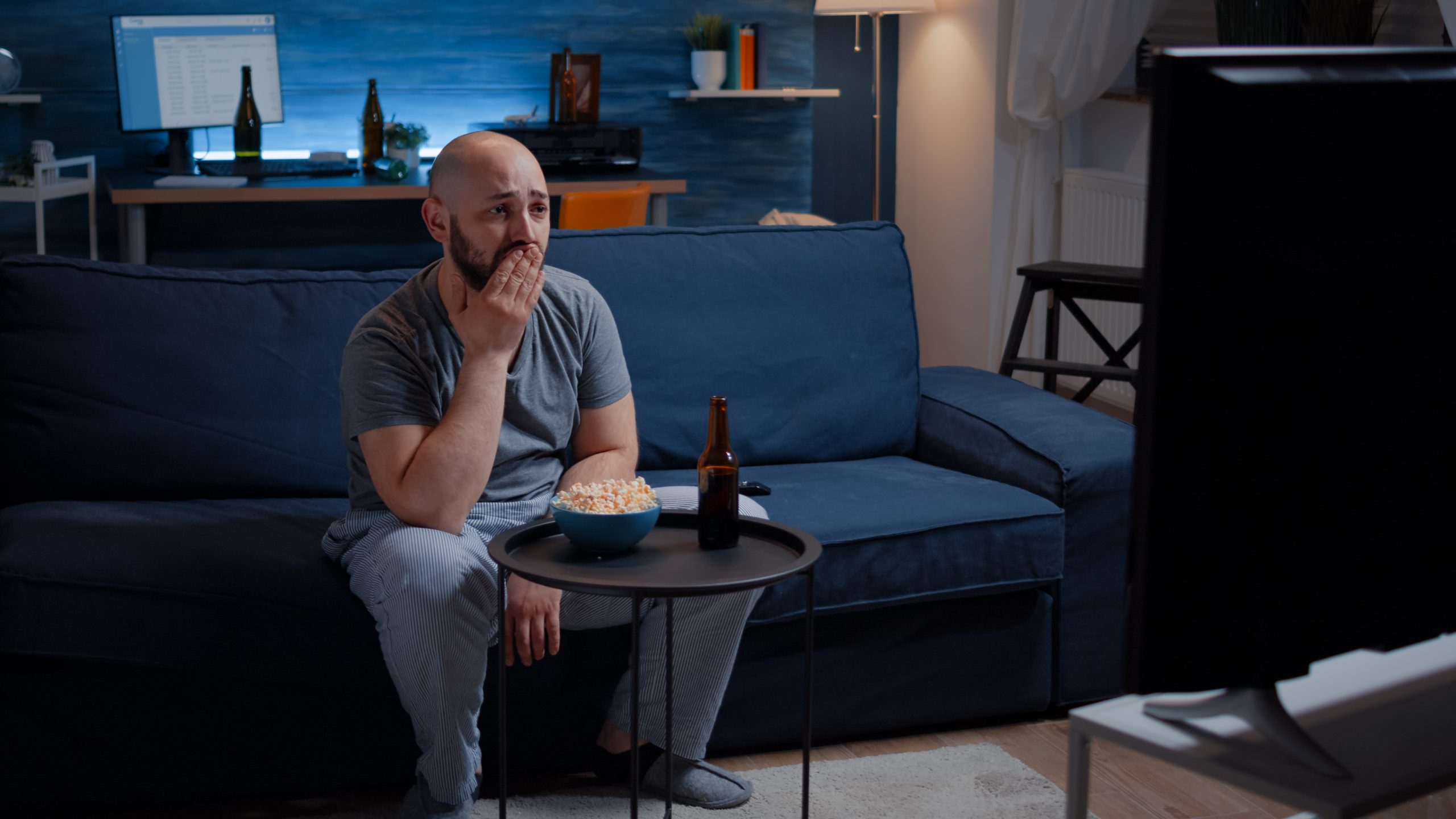 Focused man looking at drama movie, crying sitting on sofa eating popcorn